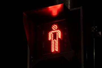 Red pedestrian traffic light signal indicating "don't walk" at night. A universal symbol of stopping, safety, warning, and waiting on a dark city street.