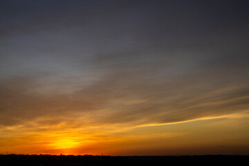 A dramatic sunset paints the sky with fiery orange and golden hues over a silhouetted landscape. The last light of day creates a serene and beautiful twilight scene.