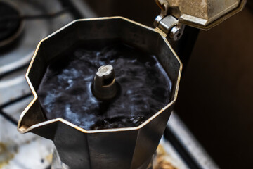 Close-up of fresh, dark coffee brewing and bubbling into the top chamber of a classic Italian moka pot, with the lid open, capturing the final moment of the stovetop preparation process.