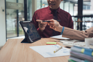 Collaboration and Insight: Two business associates exchange a pen, engaged in a discussion over a digital tablet, possibly finalizing a contract or strategizing. It is about ideas and decisions