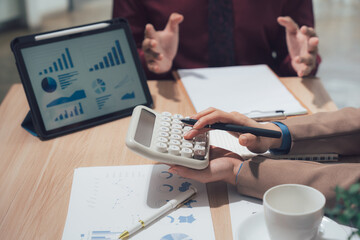 Financial Discussion: Two business people work together, analyzing charts on a tablet, calculating with calculator and discussing financial strategy. A scene of business analysis and teamwork.