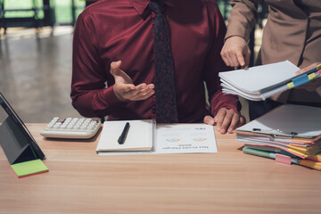 Focused Business Discussion: Two professionals engage in a focused discussion at a desk, with documents and office supplies on the table, indicating a collaborative work environment.