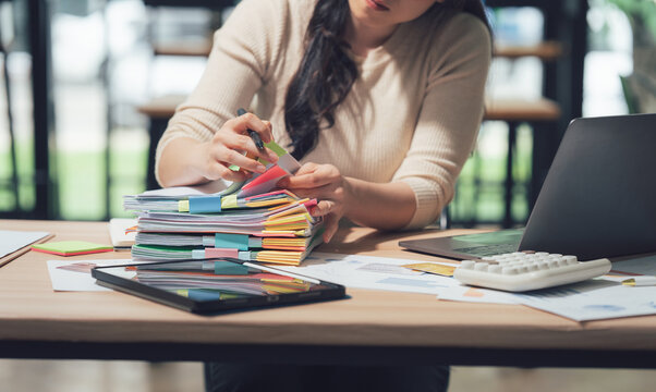 Busy Workday: A person reviews documents at a desk, surrounded by office tools, papers, and tech, highlighting productivity and focus in a professional setting.