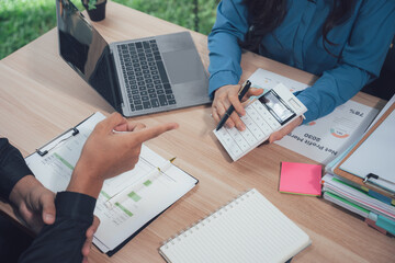 Financial Team Collaboration: A candid view of two professionals engrossed in a financial discussion, with documents, laptop, and calculator arranged on a wooden desk.