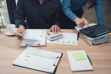 Collaboration and Focus: Two individuals engrossed in meticulous financial analysis, using calculator and digital tablet to navigate complex data, focused and precise.
