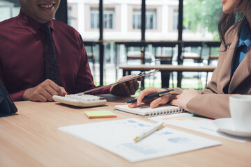 Financial Synergy: Two colleagues collaborate over documents and a calculator at a wooden table in office environment, capturing a moment of focused teamwork and financial strategy.
