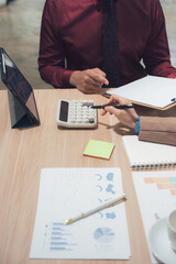 Calculating Business: Two professionals collaborate, reviewing financial data with a calculator and tablet in a modern office, highlighting strategic planning