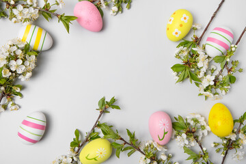 Easter colored painted eggs and blooming spring cherry branches on gray background in shape of frame with space for text and greetings. Easter and spring concept. Spring background