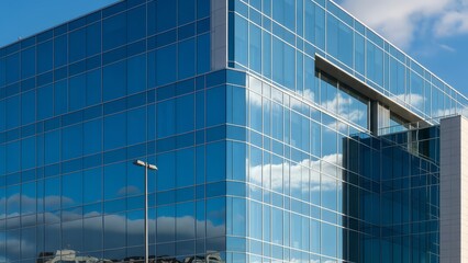 Modern glass office building exterior with reflections of blue sky and white clouds showing a contemporary architectural design on a bright sunny day with modern