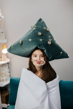 Playful girl with Christmas pillow hat indoors with candy cane