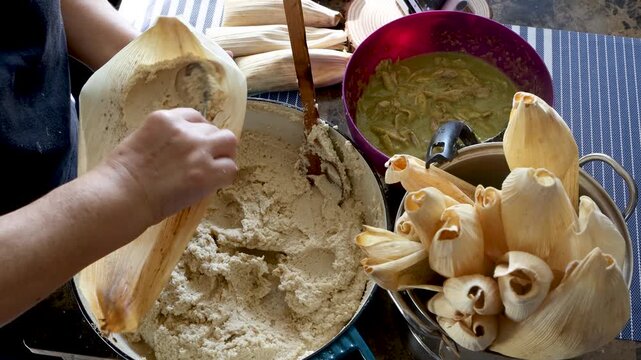 Unrecognizable woman spreading masa on a corn husk and adding chicken green chili filling
