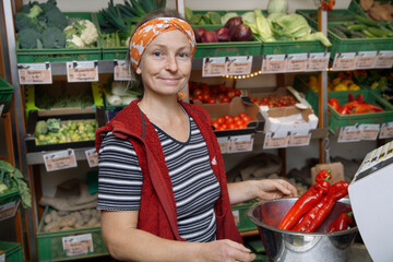 Woman smiling in biological food shop weighing red peppers