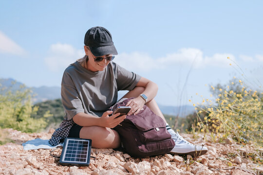 Outdoors solo traveler hiking in mountains using solar panel for digital detox