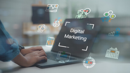 Marketer hands using laptop with Digital Marketing hologram interface, featuring SEO, social media, and advertising icons for online business strategy and growth concept in office.