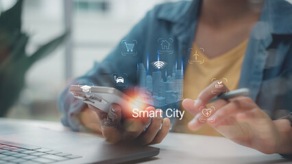Close up of hand holding smartphone with Smart City hologram interface, featuring IoT icons for urban planning, renewable energy and connected infrastructure in modern workspace.