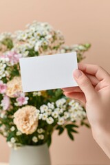 closeup of a woman hand holding a blank white business card, mockup. a beautiful bouquet of flowers is in the background