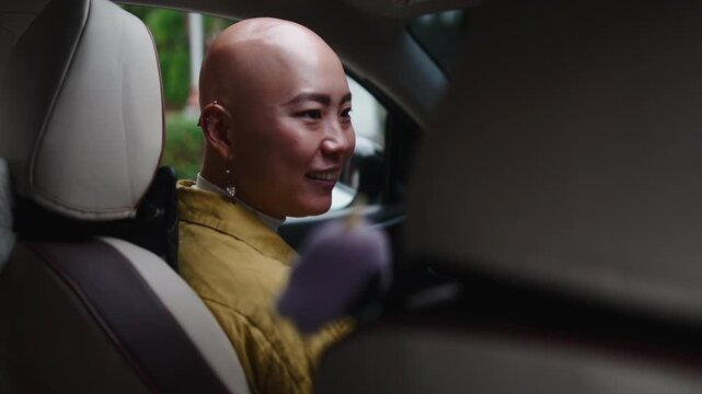 Bald asian woman smiling and talking while driving a car