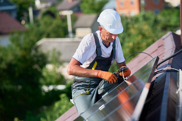 Worker installing solar panels system on rooftop of house. Electrician in helmets wiring solar modules together for generating electricity through photovoltaic effect. Concept of renewable energy.