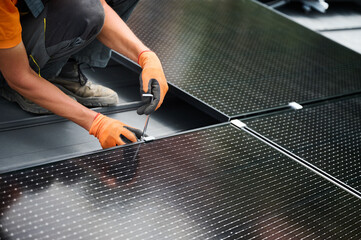 Worker building photovoltaic solar panel system on rooftop of house. Close up of man engineer in gloves installing solar module with help of hex key outdoors. Renewable energy generation concept.