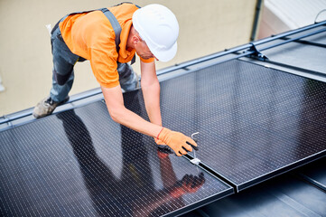 Worker building photovoltaic solar panel system on rooftop of house. Man engineer in helmets and gloves installing solar module with help of hex key outdoors. Alternative energy generation concept