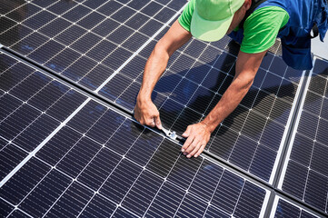Worker building photovoltaic solar panel system on rooftop of house. Close up of man engineer installing solar module with help of wrench outdoors. Alternative and renewable energy generation concept.