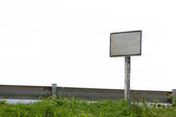 Blank outdoor advertising billboard on a green grass field by a city street under a clear blue sky with empty space for a marketing message