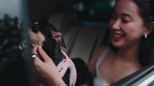 Asian woman cuddling her small dog in a car