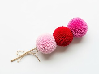 Colorful pompoms in pink and red with a gold string on a white background for decoration or craft projects