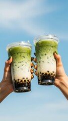 Two Hands Holding Refreshing Iced Matcha Bubble Tea Against a Clear Blue Sky