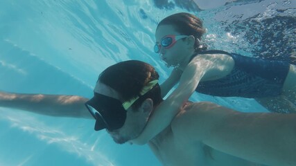 Girl swims underwater in the pool with her father. Pre teen girl feels herself comfortable and relaxed underwater while gliding piggyback on her father. Family enjoys the swimming pool