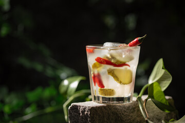 Pickle juice or brine in a glass and  pickled cucumbers and  jalapeno pepper on dark background.
