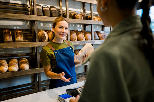 Shop assistant in bakery selling bread to client at counter