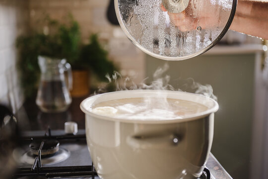 Man lifts lid from steaming pot while cooking in kitchen