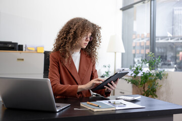 Obraz premium Professional woman using tablet at modern office desk, reviewing documents and business data, representing digital workflow, analysis, productivity, management, planning, corporate efficiency