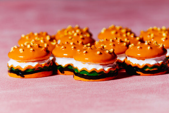 Row of toy mini burgers with bright orange tops on pink surface