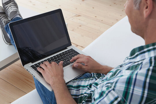 Man in plaid shirt using laptop on white couch at home in Munich