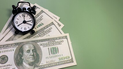 Several US hundred dollar bills with a black alarm clock, symbolizing time management, financial planning, and monetary value, concept photo