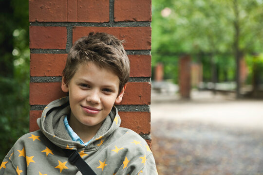 Smiling youth in hoodie with star pattern outdoors by brick wall in Berlin