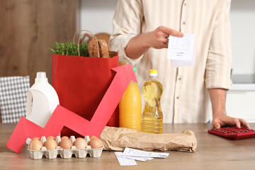 Young man with food products using calculator in kitchen. Price rise concept