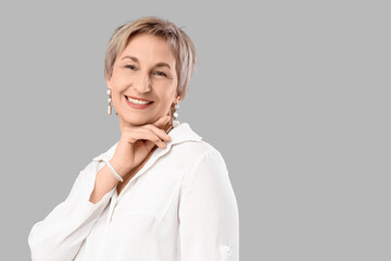 Blonde mature woman with short hair in white blouse on grey background