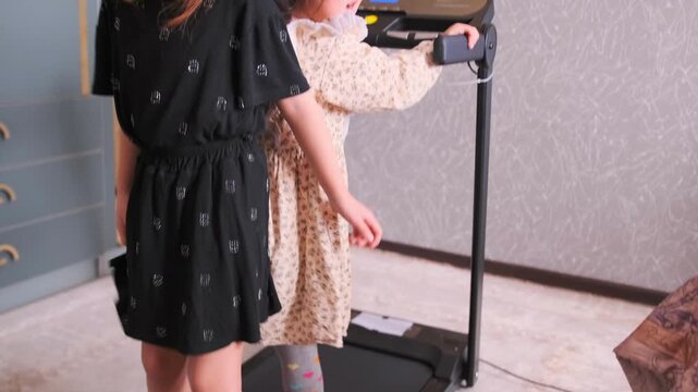 Two little Asian sisters argue and play with a treadmill at home. Emotional childhood moment with siblings rivalry, playful dispute, and lively interaction in a cozy family setting.