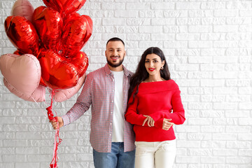 Young couple with heart-shaped balloons on white brick background. Valentine's Day celebration
