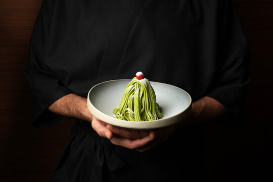 Chef presenting a gourmet Matcha Mont Blanc dessert on a ceramic plate