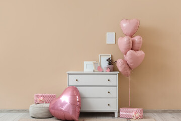 Interior of living room decorated for Valentine's Day with commode and pink balloons
