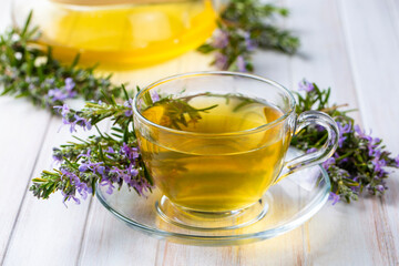 Cup of healthy rosemary tea with fresh rosemary bunch on rustic background, winter herbal hot drink concept, salvia rosmarinus
