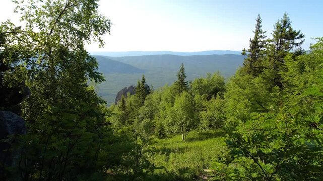 A picturesque summer landscape capturing a panoramic view of the lush green forests and rolling hills of the Southern Urals region in Russia, specifically near the Aygirskie rocks.