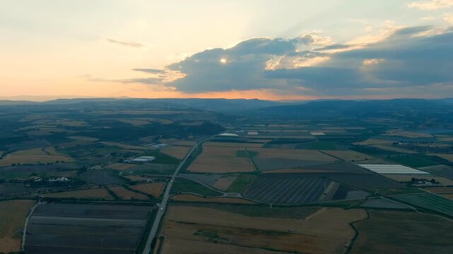 Ginosa, Italy. Geometric agricultural fields of different shades in the light of the sun breaking through the clouds. Evening time. Drone footage