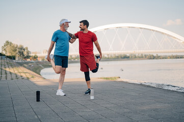 Senior man and personal trainer stretching legs after workout by the river