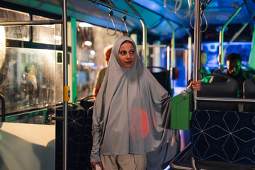 Fototapeta premium Muslim woman wearing hijab standing on a bus at night