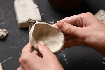 Hands of female sculptor shaping clay plate on black grunge background, closeup
